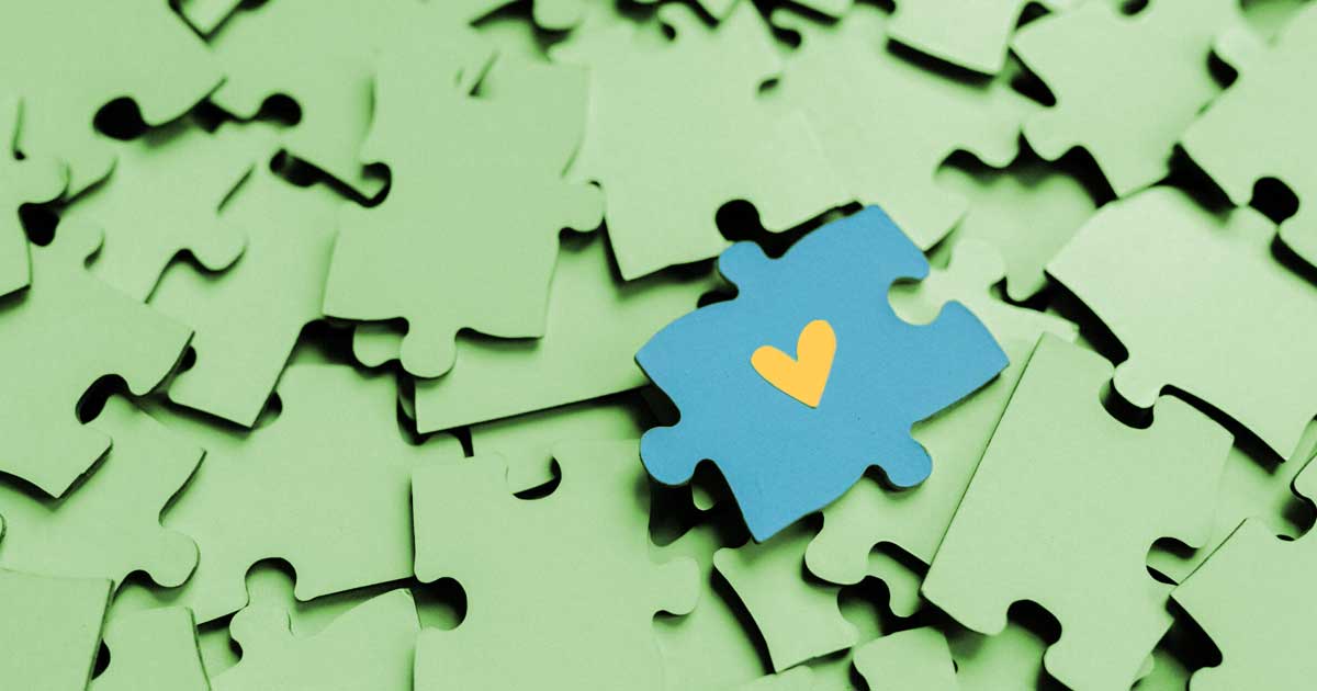 A single blue puzzle piece with a heart amid scattered pieces, symbolizing connection.